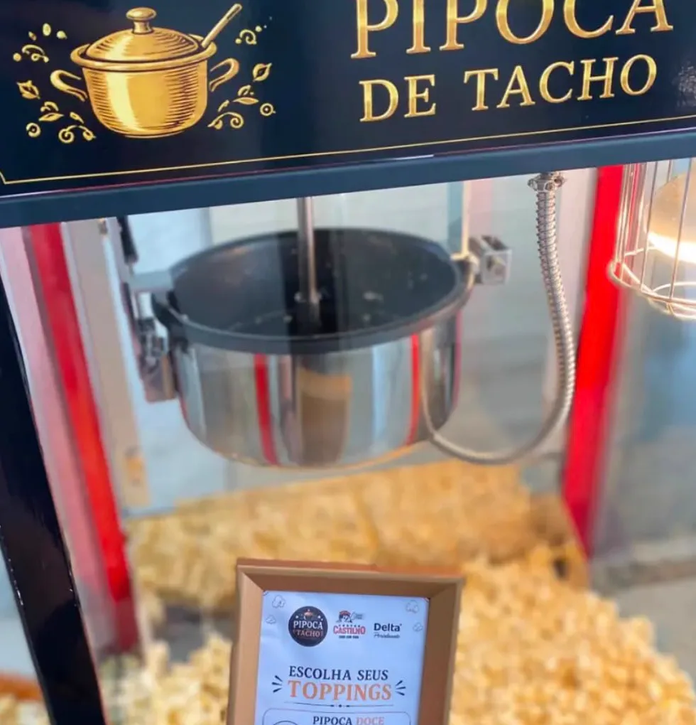 Máquina de pipoca com tacho de inox e o cardápio de toppings em moldura dourada